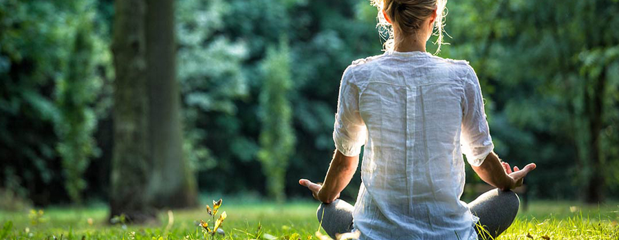 Mediterende vrouw in wit shirt op zonnig grasveld, rug naar ons toe en handpalmen open