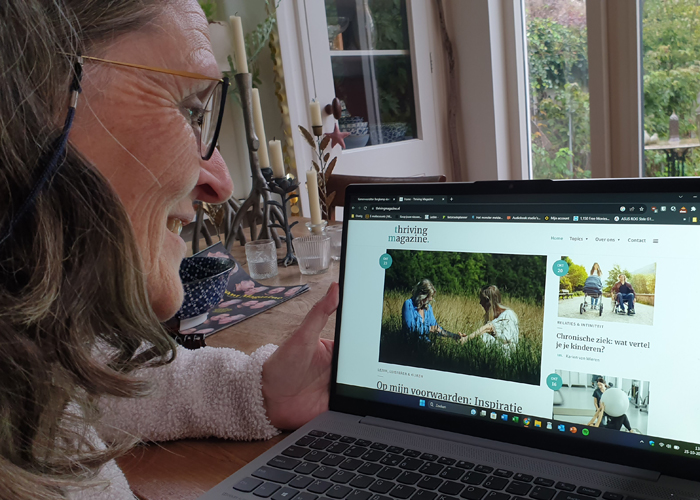 Vrouw aan tafel met laptop met daarop de website van Thriving Magazine